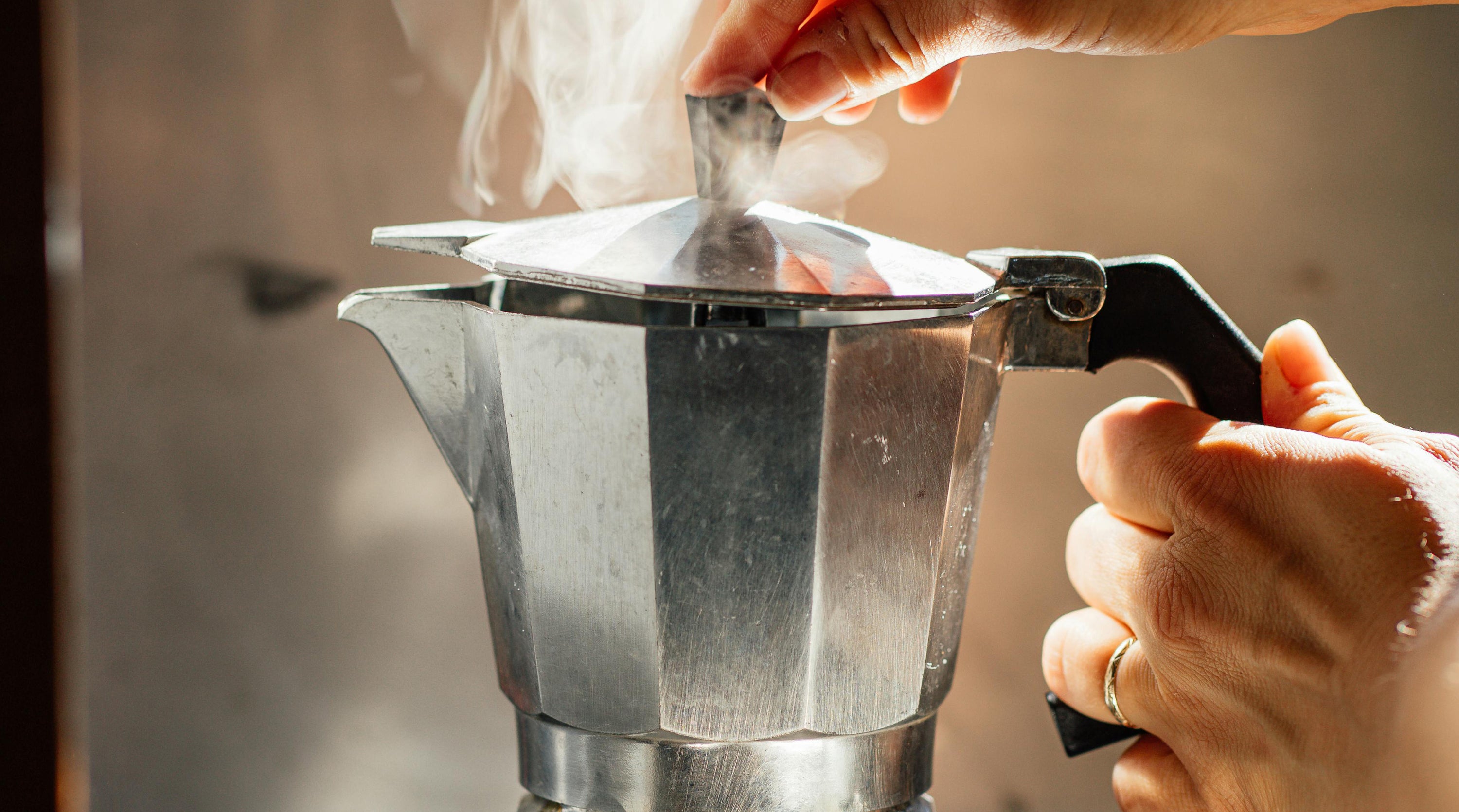 A han opening the lid of an Italian coffee maker